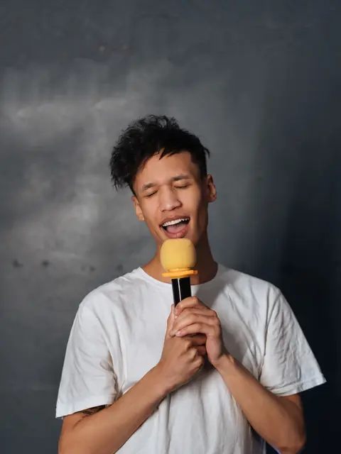 Chàng trai áo phông trắng nhắm mắt hát say sưa bên chiếc micro màu vàng.