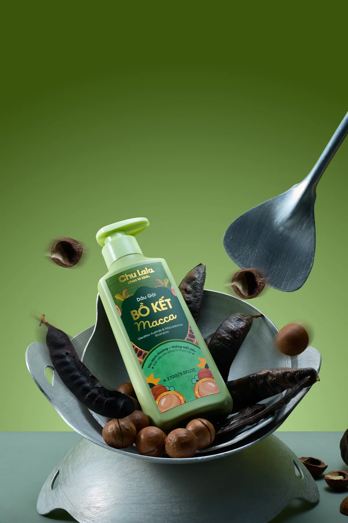 Chai dầu gội Chu Lala Bồ Kết Macca đặt trong chiếc chảo cùng quả bồ kết và hạt mắc ca