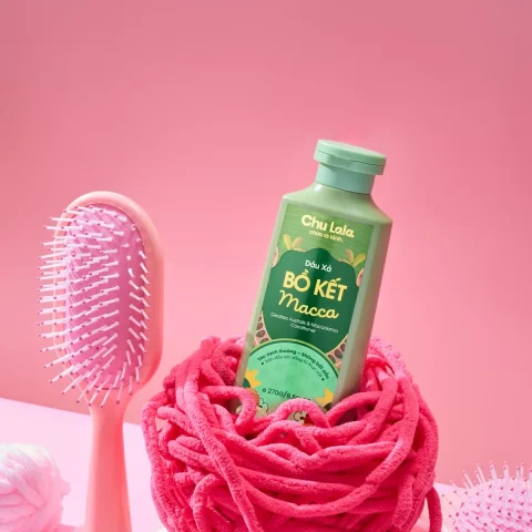 Chai dầu xả Chu Lala đặt trên cuộn len hồng, cạnh chiếc lược hồng