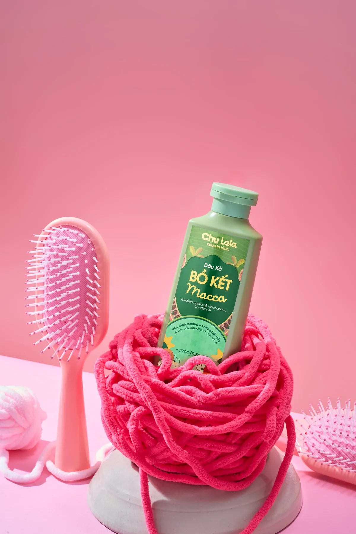 Chai dầu xả Chu Lala đặt trên cuộn len hồng, cạnh chiếc lược hồng
