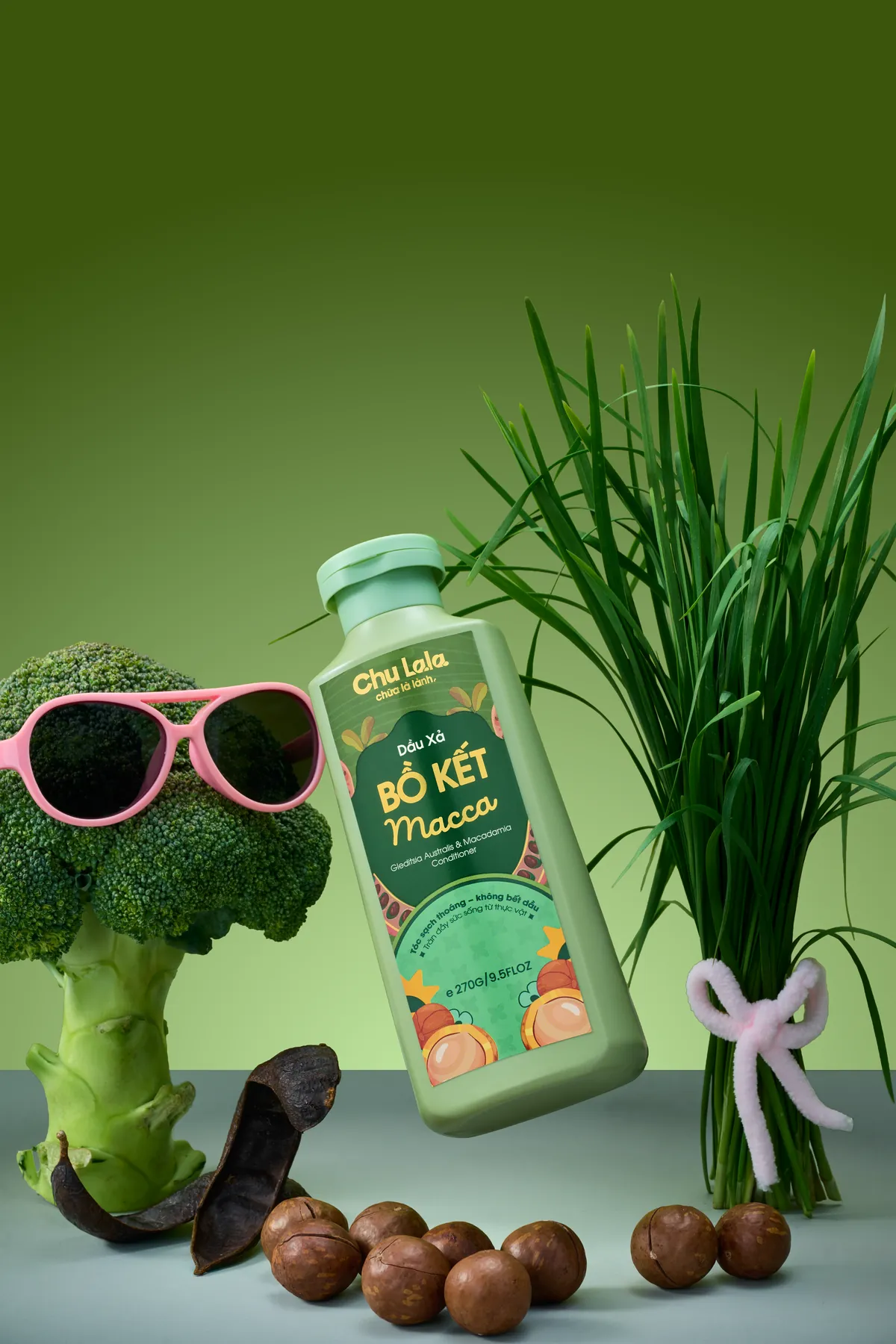 Chai dầu xả Chu Lala Bồ Kết Macca bên cây bông cải đeo kính râm và hạt mắc ca